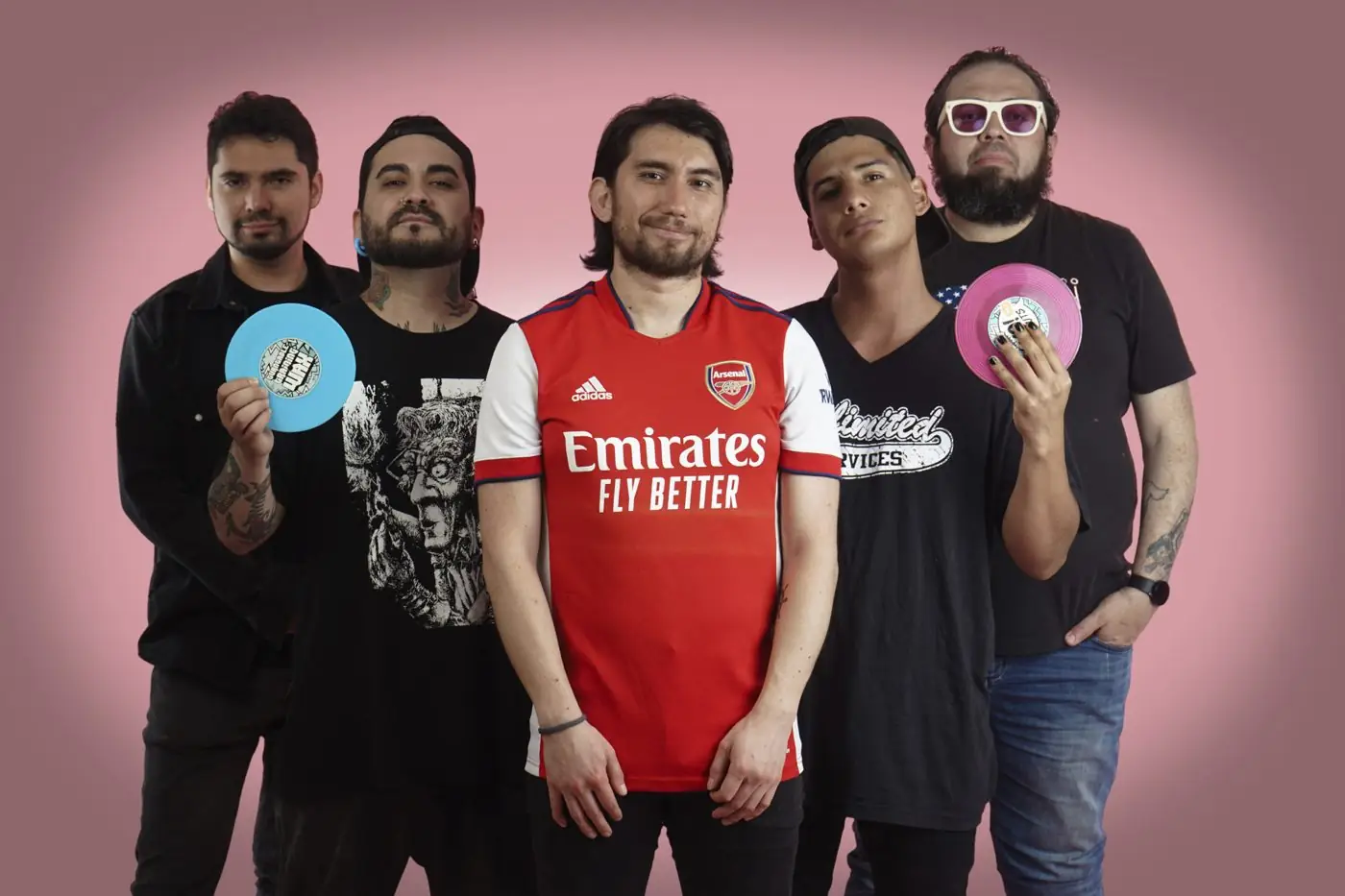 Los integrantes de la banda posando con joysticks y vinilos de colores sobre fondo rosado
